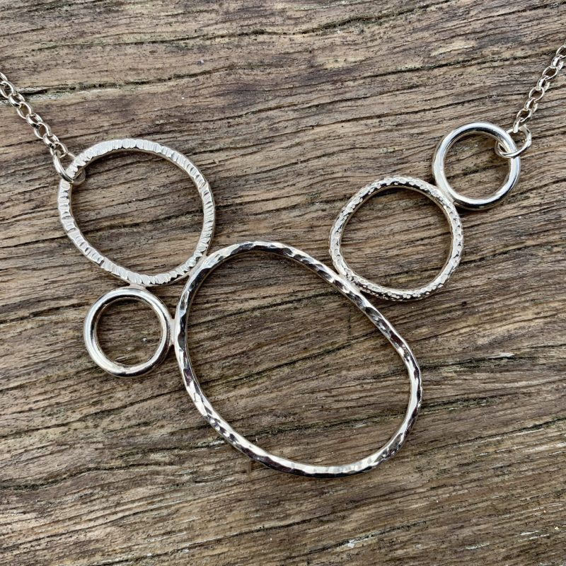 Silver necklace featuring five organically shaped circles with contrasting surface textures.