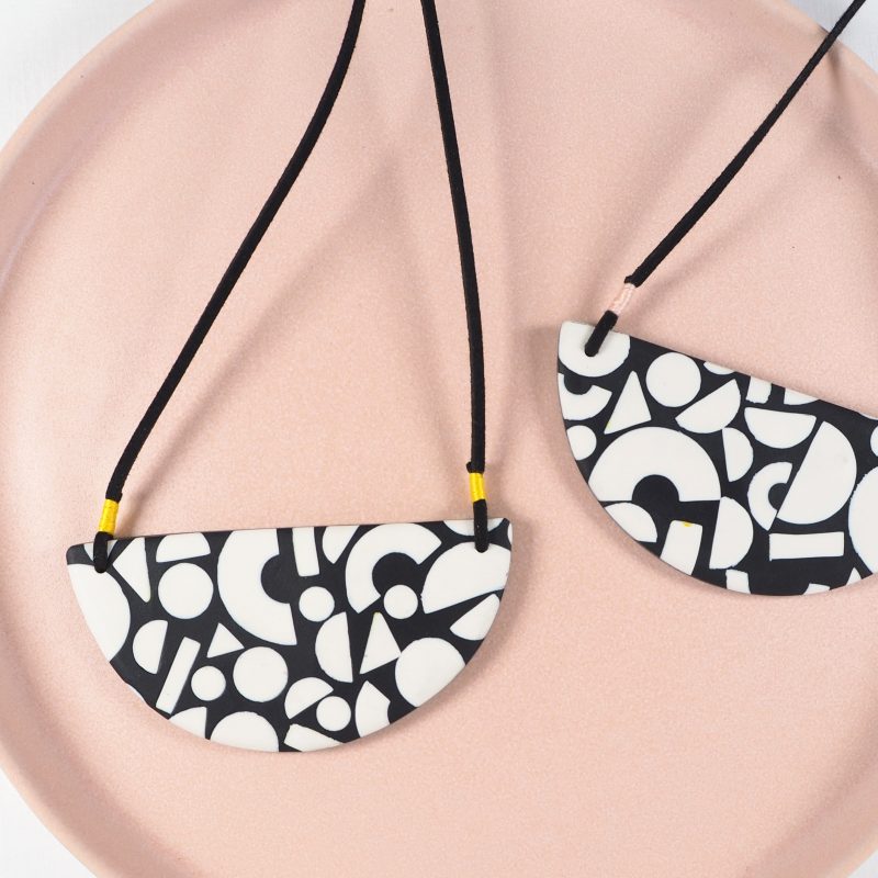 A photo of two black polymer clay bib necklaces featuring off white geometric shapes.