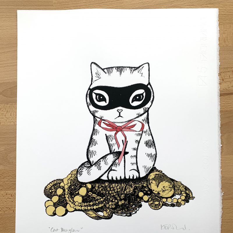 A screenprint: A masked kitten with a red bow sits atop a pile of golden jewellery