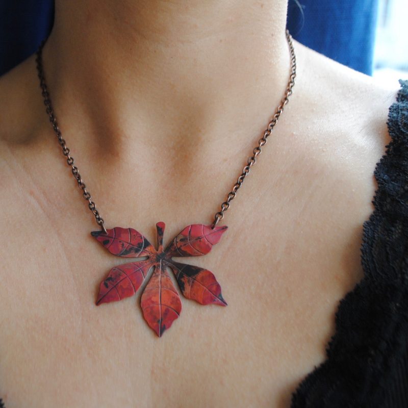 A realistic red and black Virginia creeper leaf necklace worn on the model