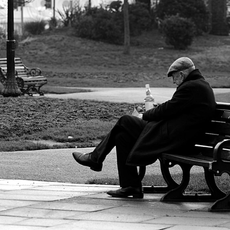 A black and white photo man is sitting on a park bench 