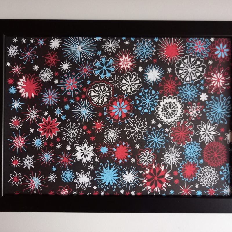 Red, white and blue sparkling abstract image using gel pens on a black background. Lots of small individual star or firework-like shapes which create a larger pattern covering the whole page.