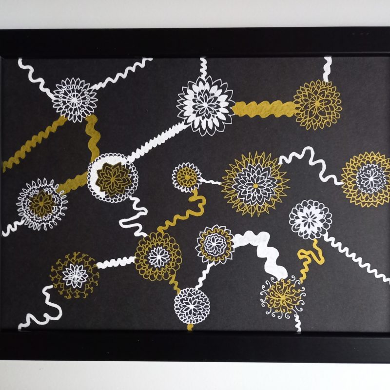 Gold and white drawing using gel pens on black card. Flower-like shapes connected with squiggly swirly lines. Image stands out on black background. 