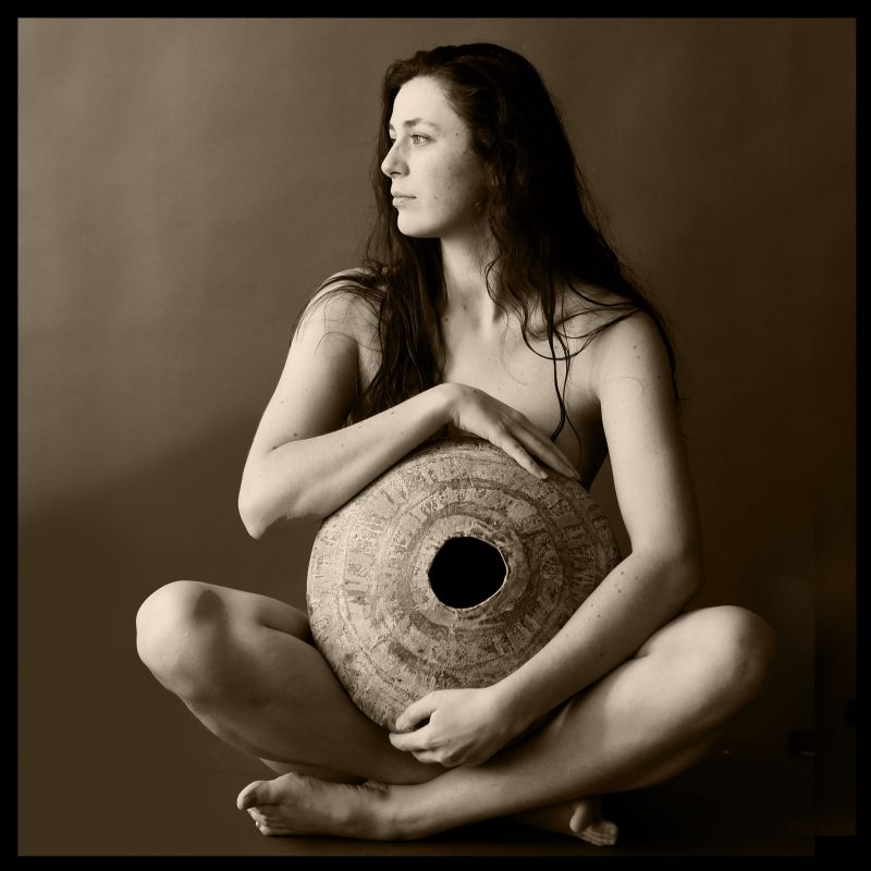 sepia toned image of a girl with a large pot as her belly as if pregnant