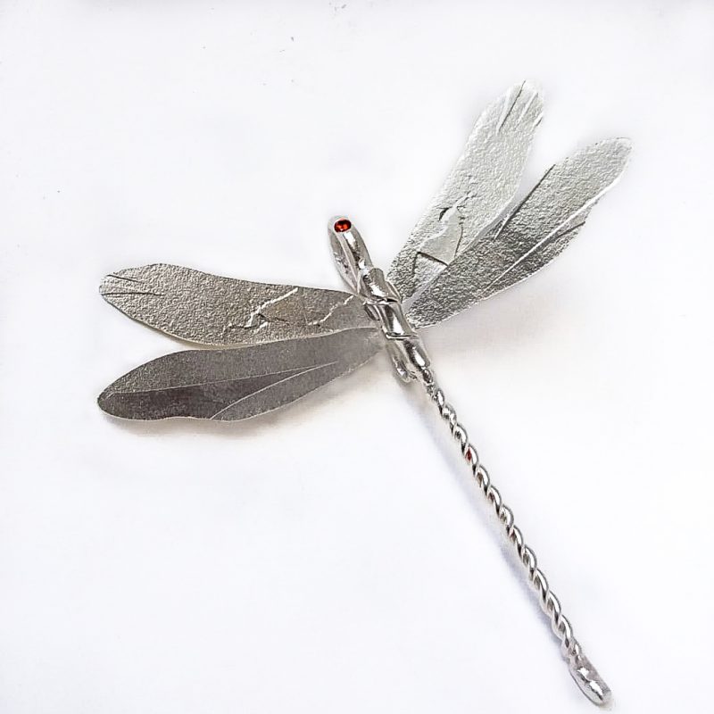 A silver dragonfly with a sparkling stone in the head that can be worn as a pendant or brooch. The wings are  textured in unique ways.