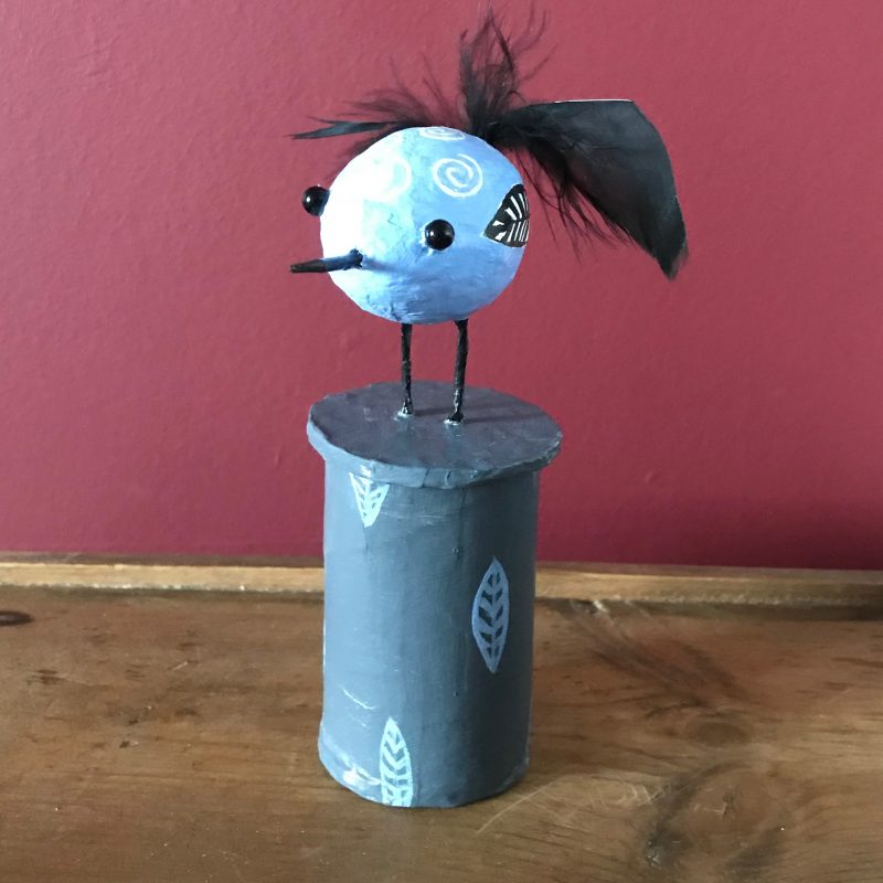 Quirky blue bird with black tail feather on decorated box plinth 