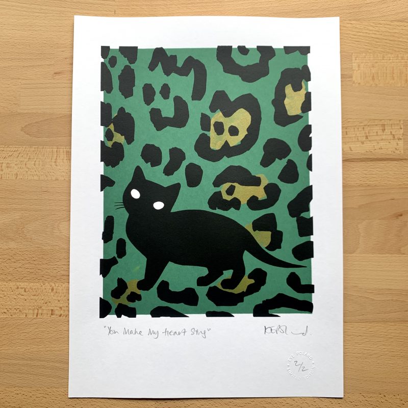 A screenprint: a large black kitten silhouette on a sage green background overlaid with gold spots and black leopardprint