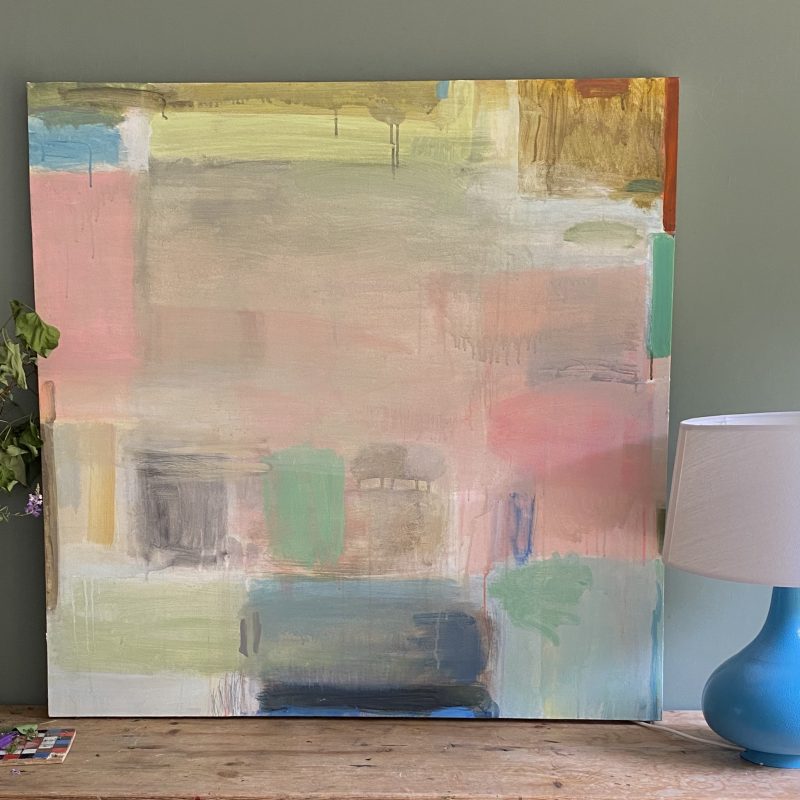A quite large painting in soft pale colours is leant against an olive green wall - its an airy uplifting abstract painting