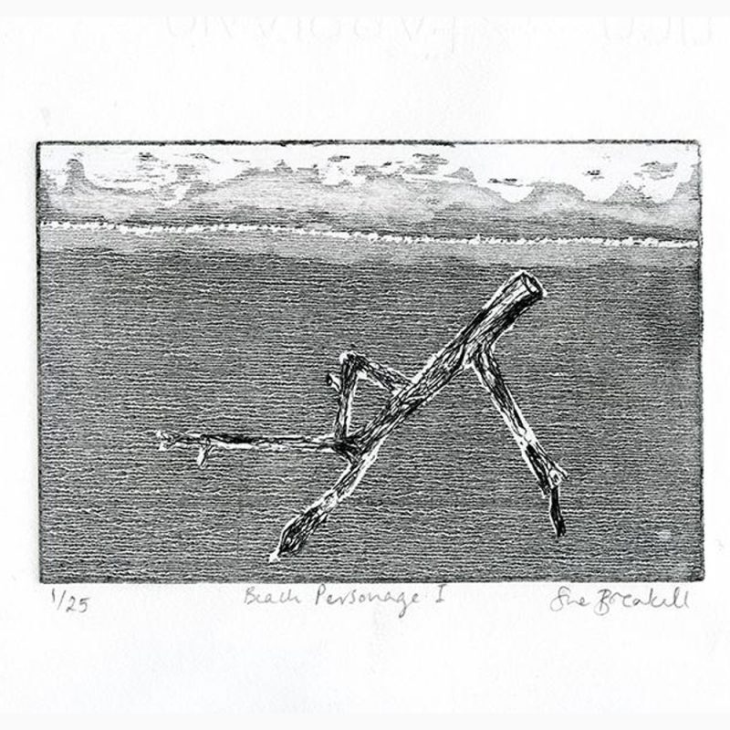 A driftwood trunk and branches, resembling a human figure in its arrangement of 'limbs', on a beach with distant waves and sky.  Printed in black ink on off-white paper