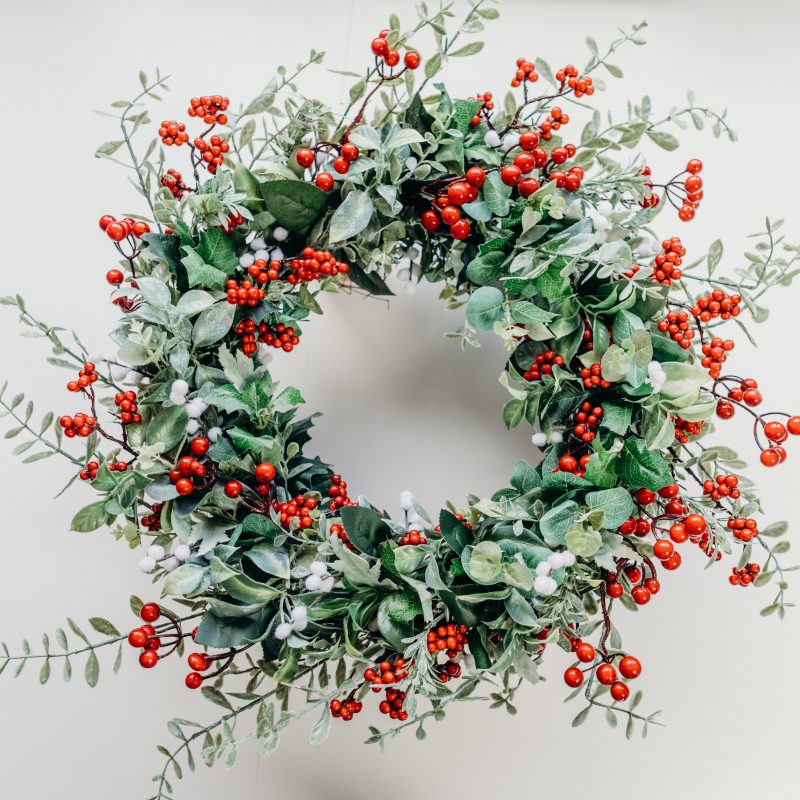 A beautiful Christmas wreath created with a variety of green foliage including holly and eucalyptus, red berries and white mimosa. This wreath is perfect for hanging on the front door, as a wall hanging or as part of a table centre piece with candles. 
