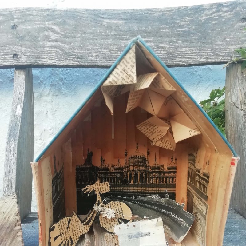 Cardboard house box made of book covers with paper cut illustration of bicycle.