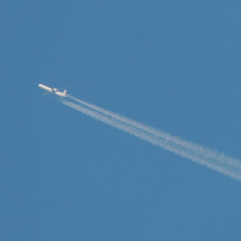 An airplane flies across the image with bright blue sky behind it