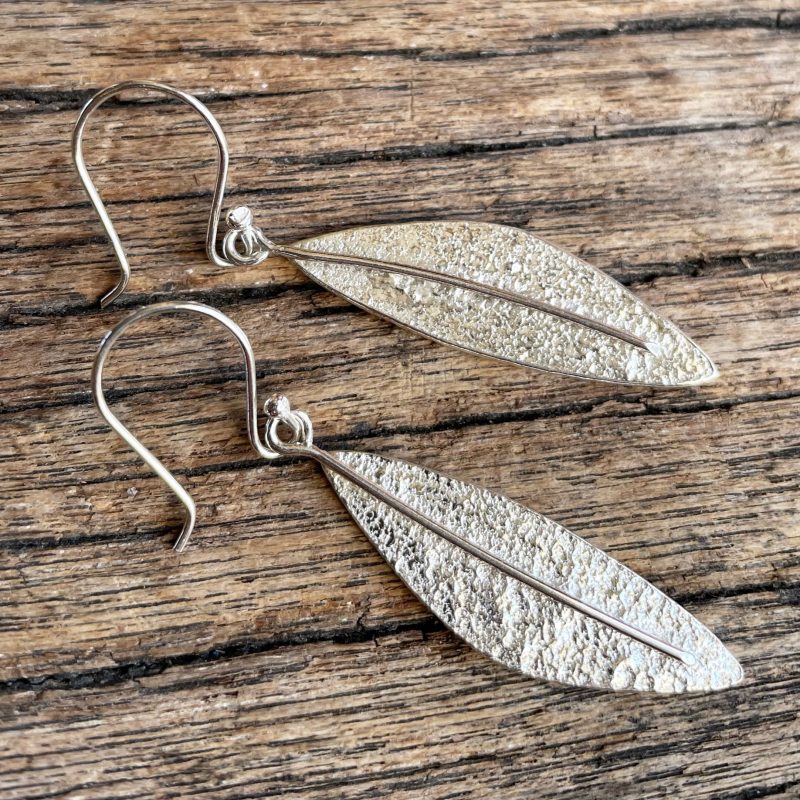 Asymmetric leaf earrings with a shiny, rustic surface texture and central vein. Hook fixing.