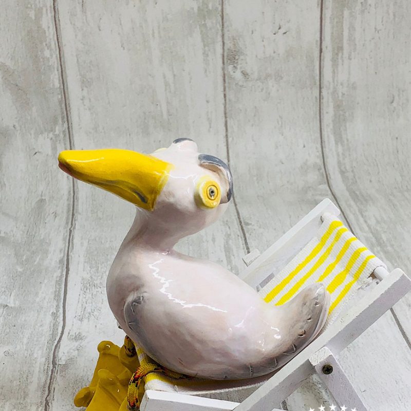 A quirky seagull sitting on a miniature deckchair with movable legs made from paracord and big ceramic webbed feet.