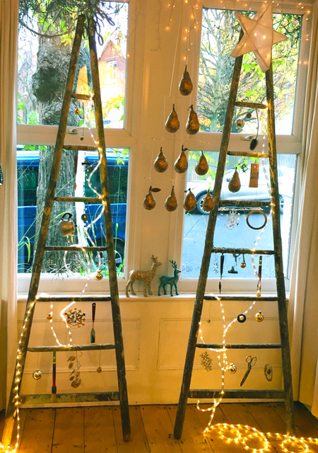 A pair of ladders stand in a bay window with decorations and lights on.