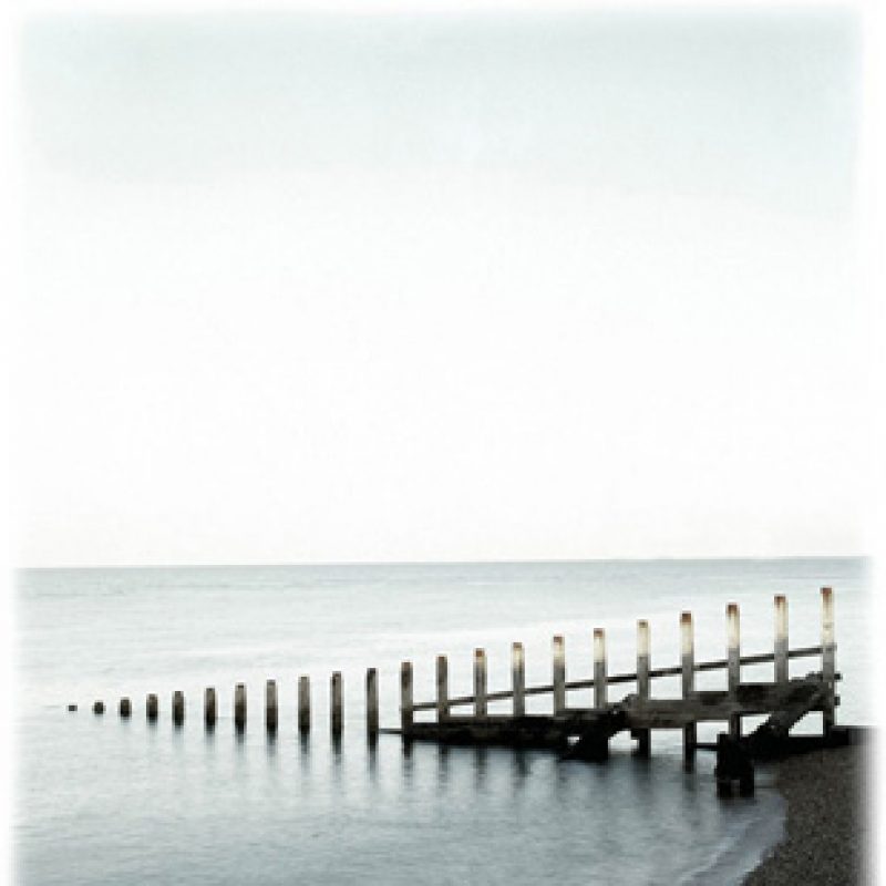 A calm serene sea with a line of wooden sea breaks and a grey calm sea behind