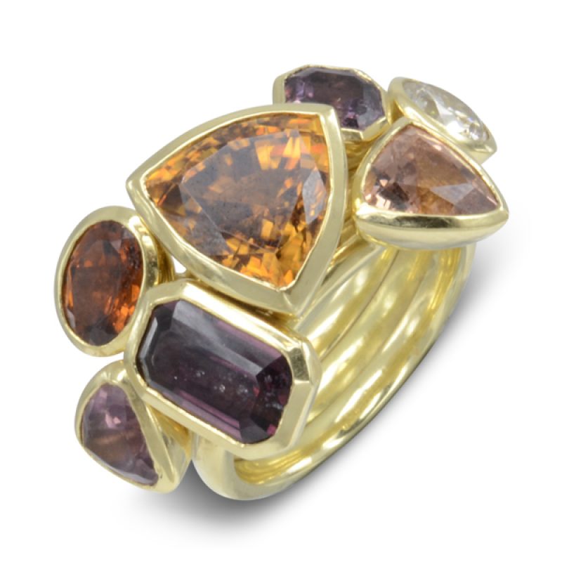 A Giant Stacking Cocktail Ring featuring a 5ct Trillion Natural Brown Zircon, 6mm round pale yellow fancy diamond, emerald cut purple spinel, trillion cut pink spinel, octagonal cut purple spinel,  and an oval orange garnet and a trillion champagne garnet. Handmade in 18ct yellow gold this unusual bespoke ring brings together lovely rich autumnal hues.