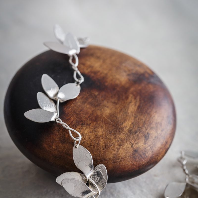 Silver jewellery in shape of sycamore leafs draped over pebble