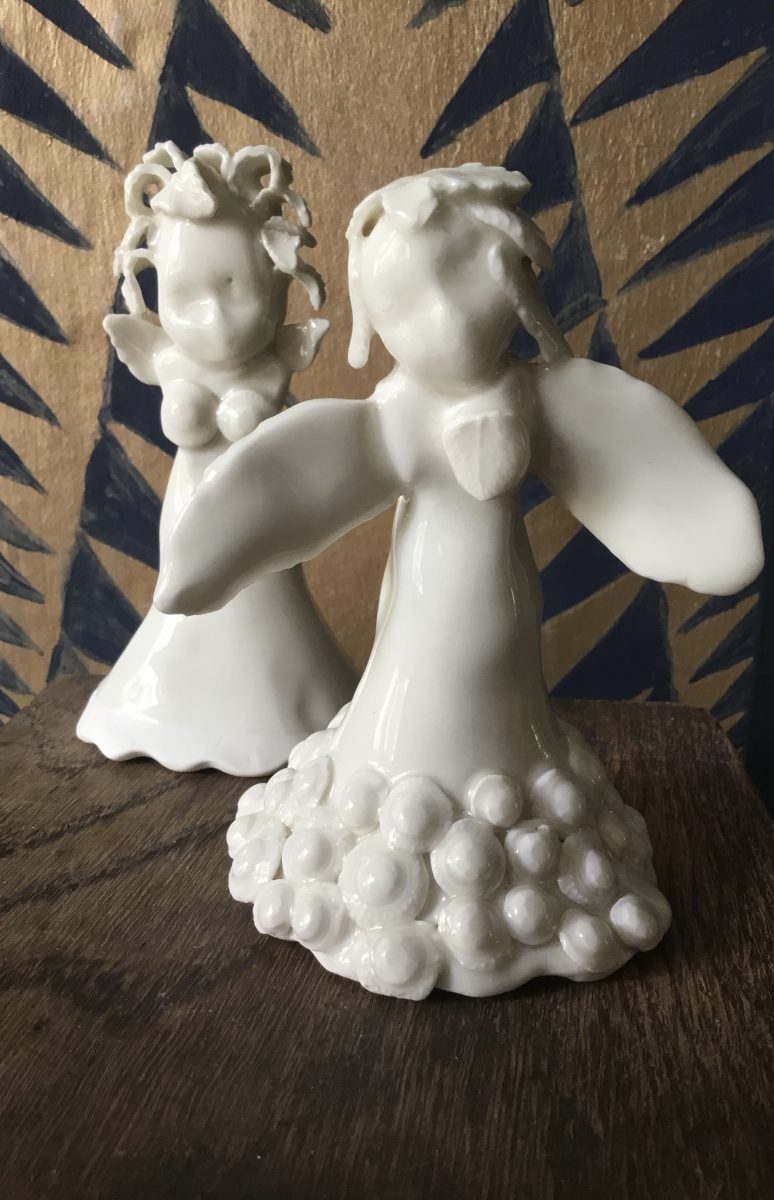 Two white porcelain angels. One with mad hair and the other wearing a detailed skirt.