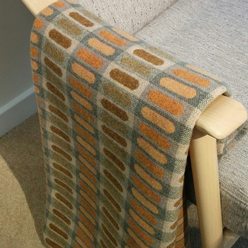 A woven throw in grey-greens and amber colours.