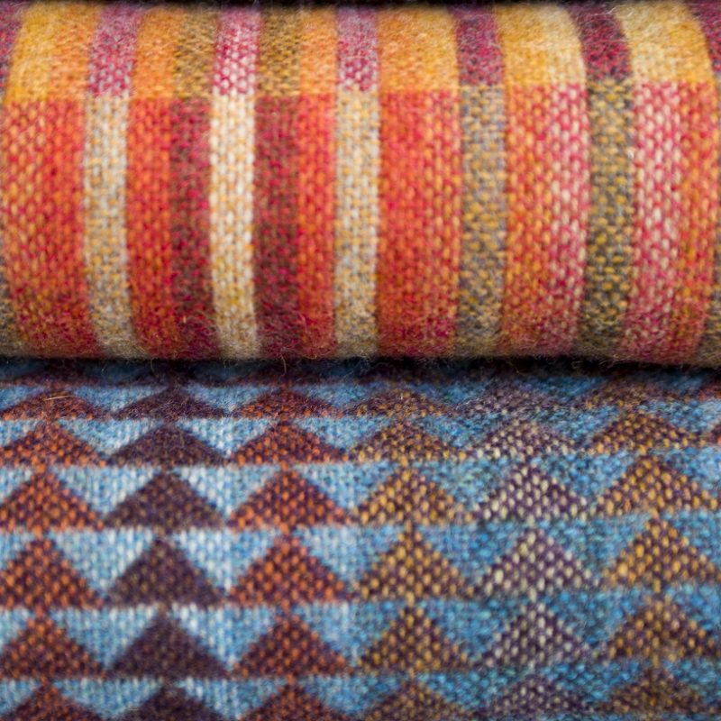 Two throws--Reeds Berry in vibrant warm colours and Jig Lapis in dark moody blues and deep claret. Stripes and triangular motifs.
