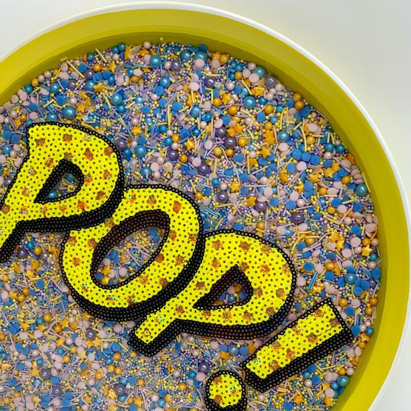 Resin Serving Tray. Unicorn rainbow sprinkles suspended in layers of crystal clear resin. Sequin yellow “POP!” sign overlaying sprinkle base. Sunshine yellow metal tray.