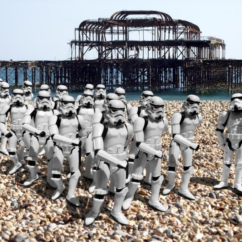 A parade of miniature Star Wars storm troopers gathered on Brighton beach, with the West Pier set in the background 