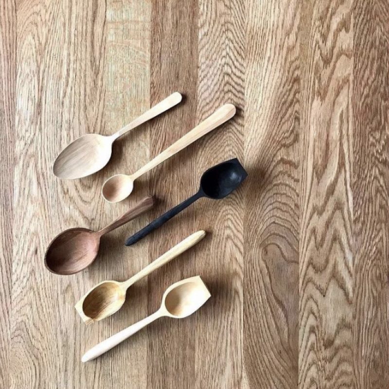 6 hand carved spoons in a variety of locally sourced woods sitting against a wooden background.