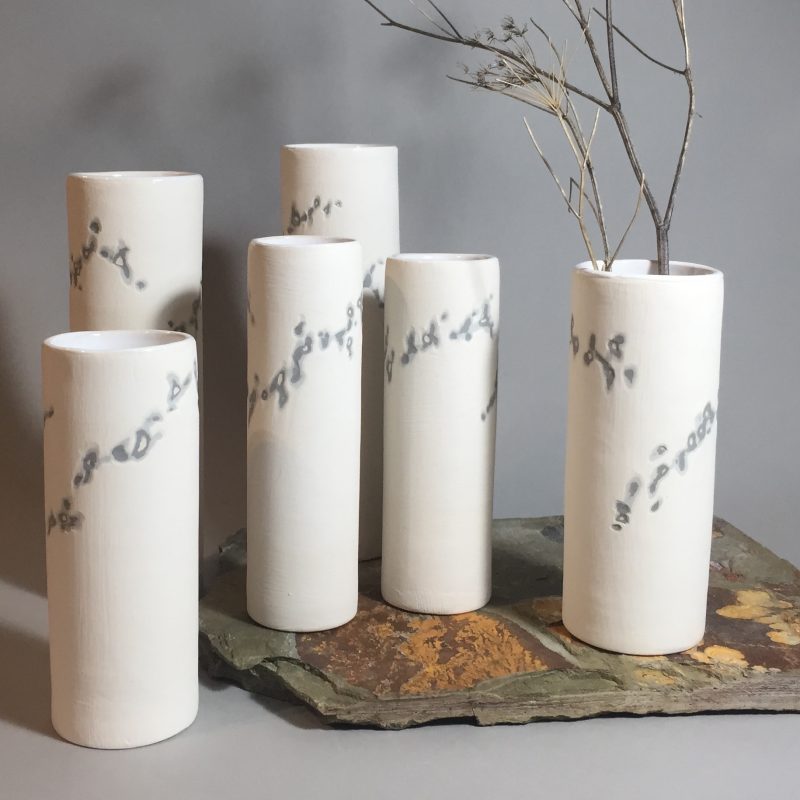 white cylindrical vases suggesting chalk cliffs, with darker patterns giving the impression of seams of flint. The exterior is matt unglazed slip, featuring the sgraffito technique, while the inside is glazed gloss white