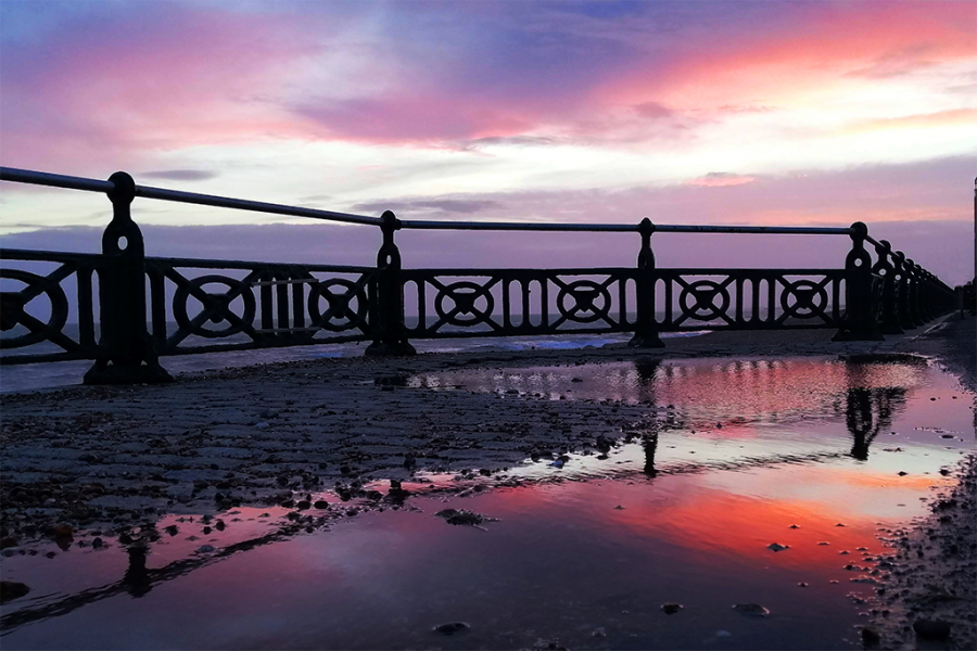 Hove promonade railings at dusk with sunset reflected in a puddle