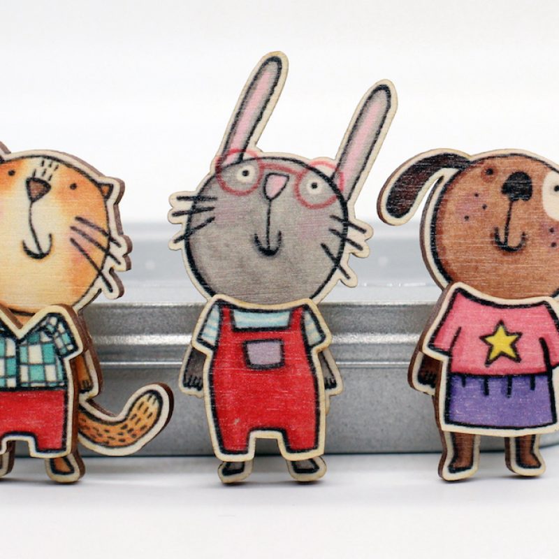  Three hand drawn character badges, a cat, a rabbit and a dog, made from printed lasercut wood, all wearing clothes