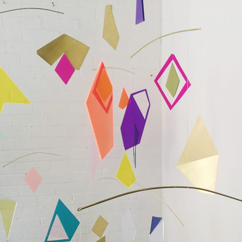 brightly coloured geometric shapes in acrylic hand from mobile arms against a white back ground.