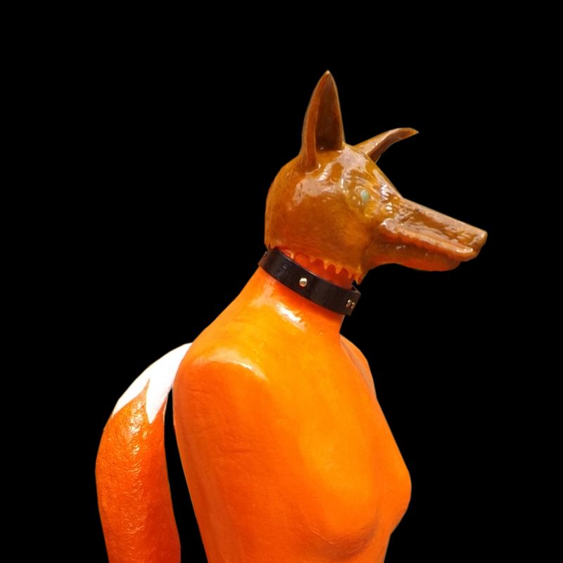 bright orange mannequin with the head and bushy tail of a fox wearing a dominatrix collar  (head illuminates)