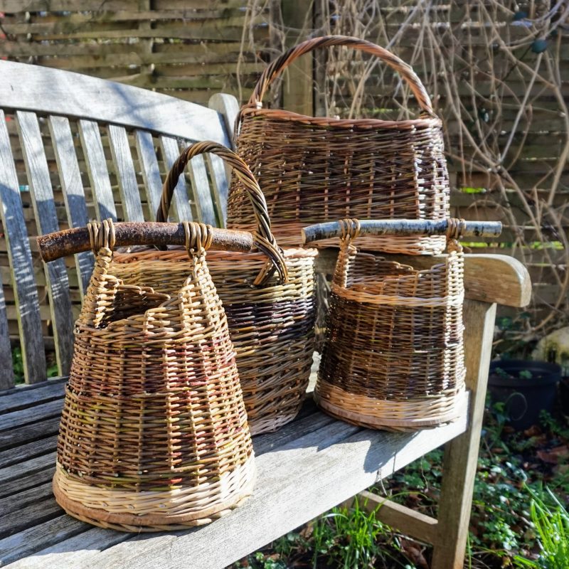 Collection of hand woven willow baskets of various cylindrical shapes with cutoff branches for handles in stripes of natural wood colours