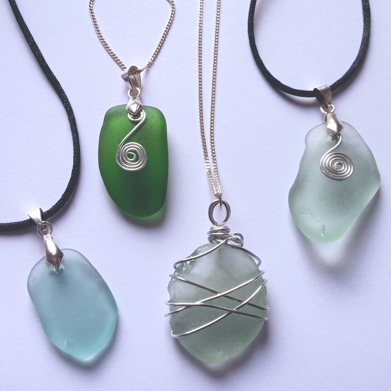 Five necklaces made from natural sea glass and metal wire hung from chains or black leather cord