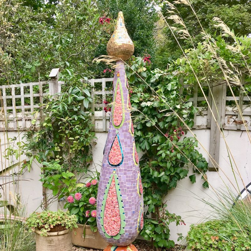 Tall slim garden sculpture. Orange base and pink top with green and gold detail.