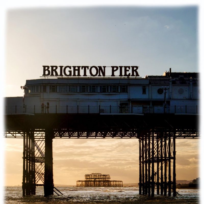 An ambient view of Brighton Palace Pier and the West Pier Ruin behind, through the pillars/legs of the Palace Pier.