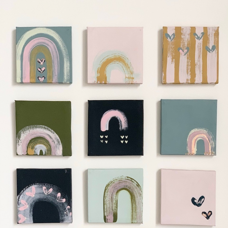 12 mini rainbow canvases arranged in a grid on a white background. Each canvas is painted with muted pastels and black tones featuring Adelle's signature rainbow motif.