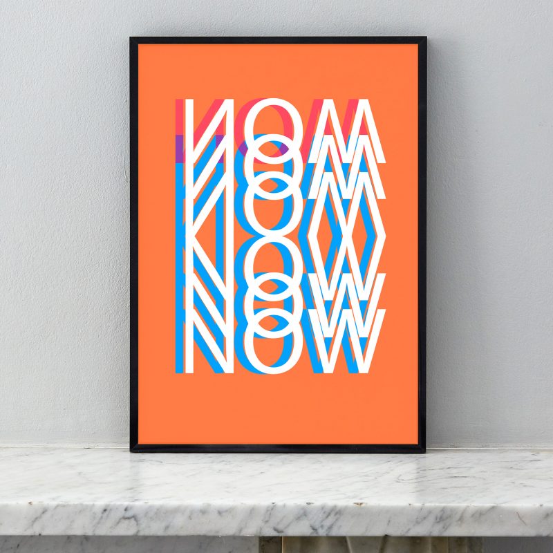 Rich background orange art print with the words NOW filling the page.  Print is framed in a black frame and sitting on a fireplace mantle.