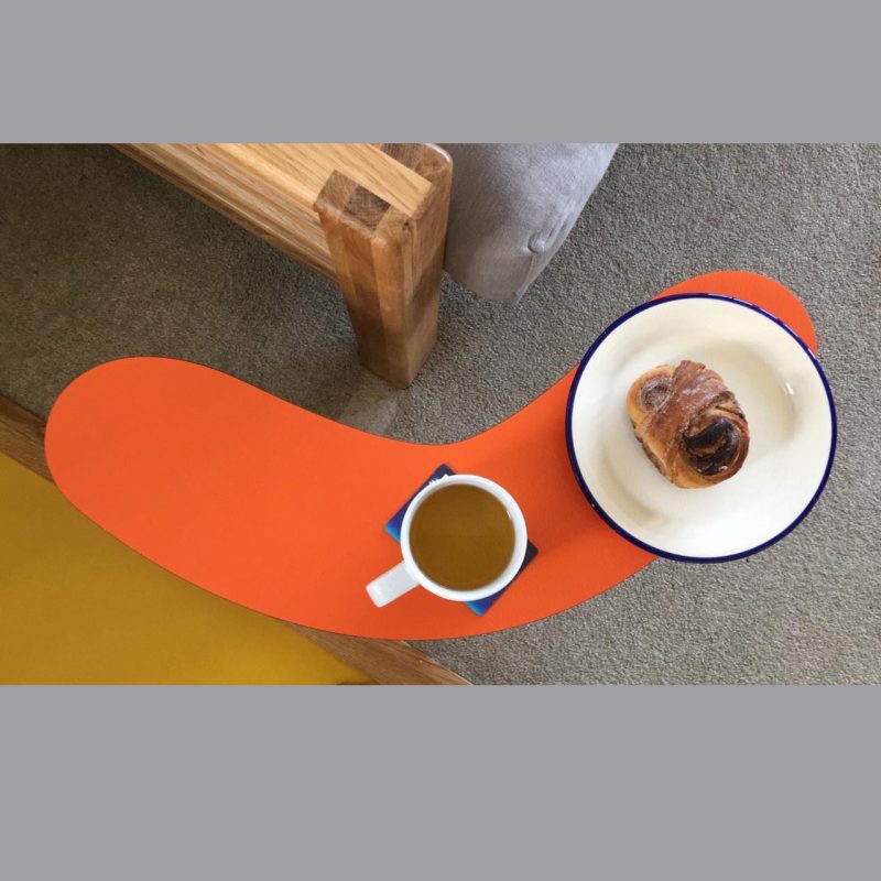 Photograph of curved orange laminate table with a cup of coffee and a croissant on it