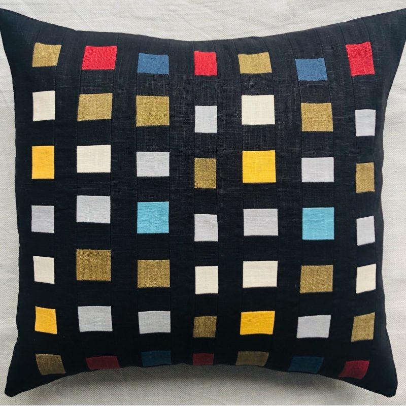 A linen cushion with a pattern of graphic embroidered colourful squares