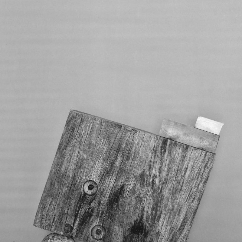Black and white photograph Large square wooden block balancing on a ball to the left 