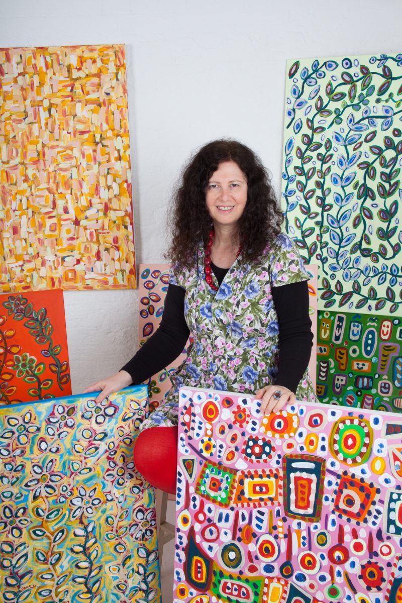 Orna standing surrounded by her colourful painting 