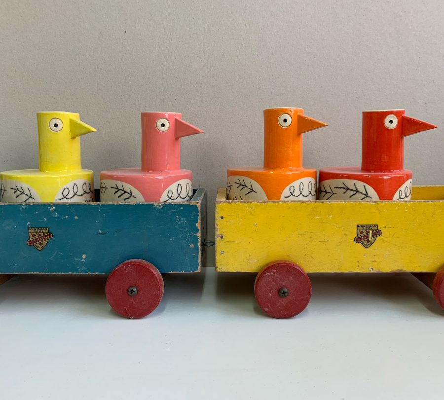 Colourful bird shaped ceramic vases placed in wooden toy train carriages 