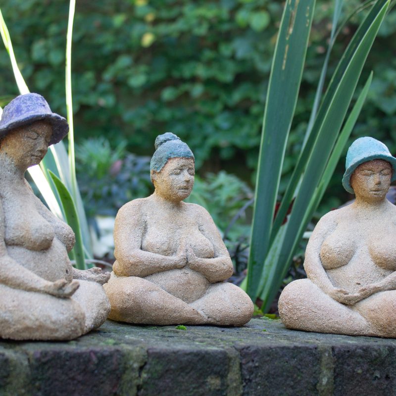 3 Budda like ladies sitting on a garden wall