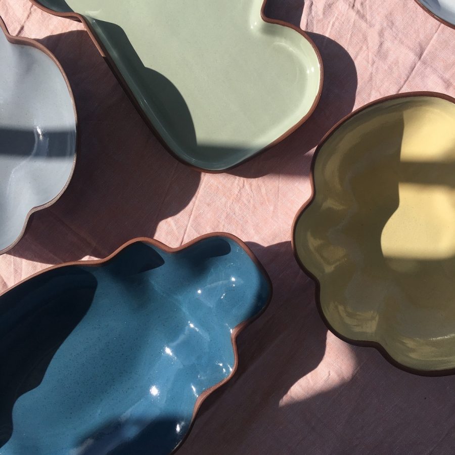 set of colourful terracotta scalloped shape bowls glazed in blue, yellow, green and grey on a pink tablecloth
