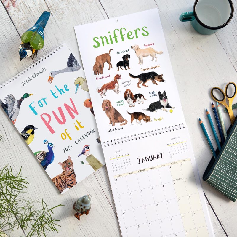 Two illustrated calendars lying on a table with props around them