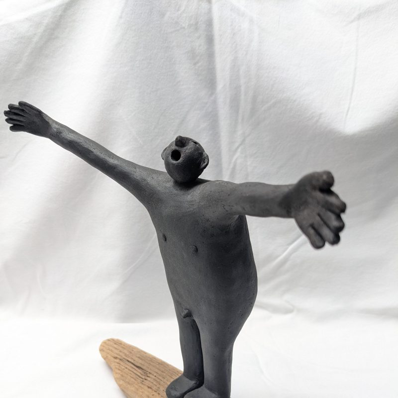 cermaic figure of man with arms out and mouth open, on driftwood base