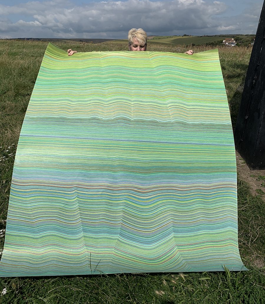 Artist Laura Waldusky with large unframed colour pencil drawing in an open field by Rottingdean Windmill.