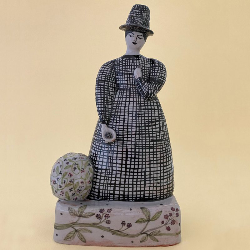 A ceramic lady in long dress and hat had decorated patterns